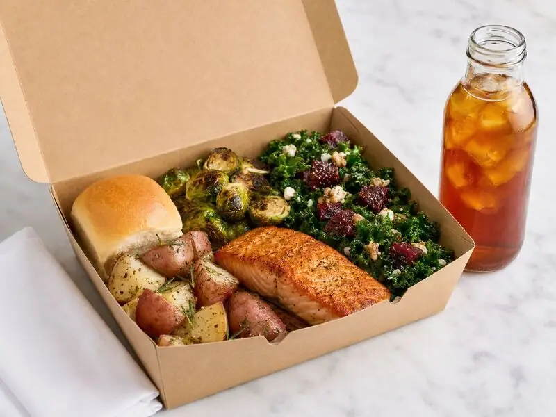 Boxed catering meal of roasted salmon, herbed potatoes, Brussels sprouts, kale and beet salad, bread and iced tea packed for a Dublin catering office delivery