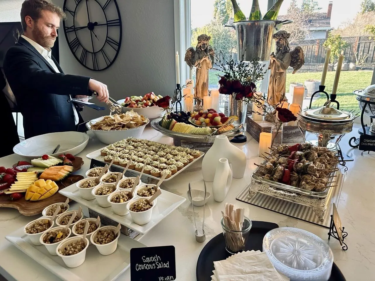 Polished starter buffet of herbed couscous salad, a fanned seasonal fruit platter and char-marked grilled skewers on crisp white linen — corporate starter menus from our Livermore catering team